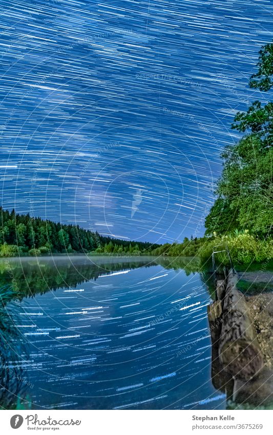 Long Exposure Startrails über einem idyllischen See mit Sternreflexionen im Wasser - wunderbare sternenklare Nacht. Startschienen Reflexion & Spiegelung