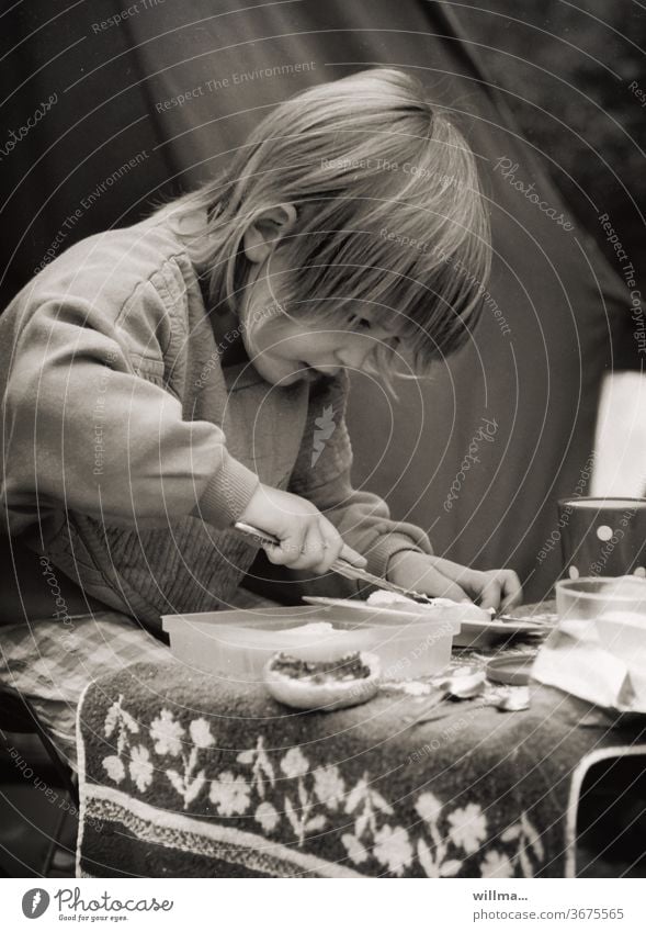 Kind beim Frühstück auf dem Zeltplatz, analoge Fotografie Camping Brötchen schmieren Messer Konzentration Zelten DDR-Zeit Frühstückselbstständig eifrig