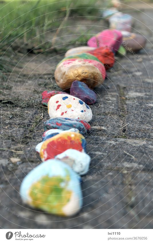 Reihe auf dem Pflaster ausgelegte bunt bemalte Glückssteine Stein in Reihe Glücksbringer kleine Kunstwerke Natur Trend Ideen Hobby lächeln basteln Zeitvertreib