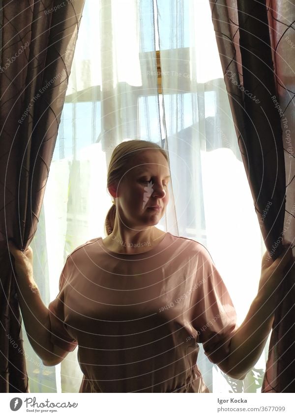 Vorderansicht einer Frau, die Vorhänge hält Fenster Beteiligung schön Schüchternheit braun Hintergrundbeleuchtung herabsehend Lifestyle Vorhang