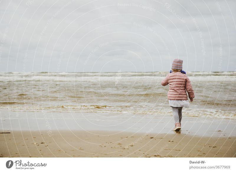 das Kind und die raue See Mädchen Nordsee Meer Wellen gehen erkunden interessiert Urlaub neugierig Wasser anziehend fasziniert anonym Rückansicht Kindheit
