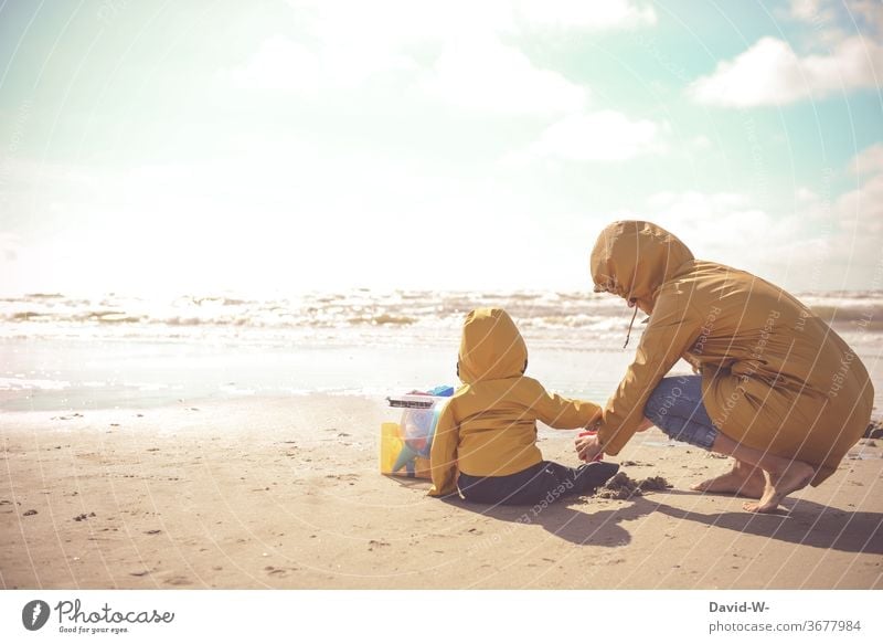 Mutter und Kind mit Friesennerz spielen zusammen am Strand Sohn Mutter mit Kind Mutter mit Sohn Stimmungsvoll Sonnenlicht Sonnenschein gelb besonders schön