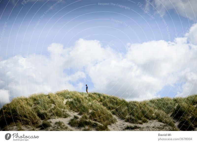 Mann steht alleine in den Dünen und genießt die Ruhe stehen genießen einsam Abstand Urlaub Wolken klein riesig landschaftsbau Landschaftsaufnahme