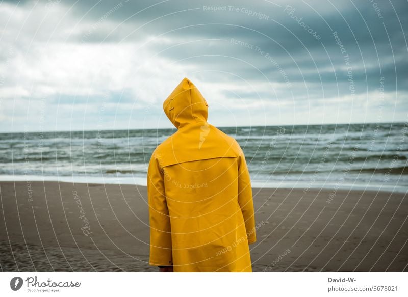 Mann spaziert mit Friesennerz am Strand entlang spazieren friesennerz Unwetter Wetter Wetterumschwung Regenjacke Himmel schlechtes Wetter Gewitterwolken gelb