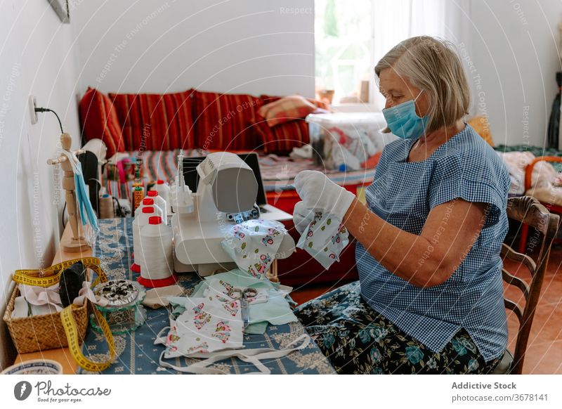 Ältere Frau näht zu Hause Schutzmasken Coronavirus Mundschutz nähen Kunstgewerbler COVID handgefertigt heimwärts Pandemie behüten selbstgemacht verhindern älter