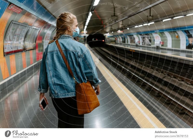 Moderne Frau in Schutzmaske zu Fuß auf dem U-Bahn-Bahnsteig Mundschutz Coronavirus Passagier Podest COVID Pandemie Infektion behüten lässig jung unterirdisch