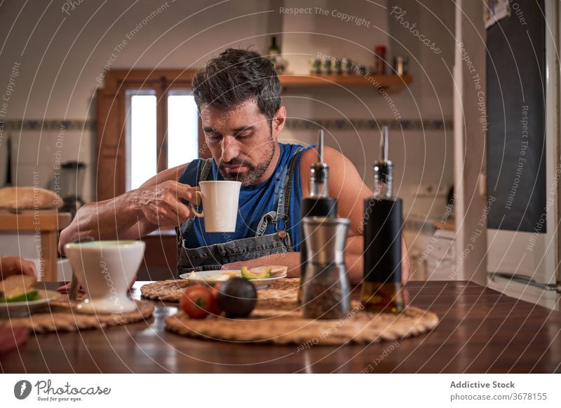 Reifer Mann beim Frühstück in der Küche essen lecker Getränk genießen Becher trinken Tasse Windstille heiß geschmackvoll heimwärts Lebensmittel Kaffee