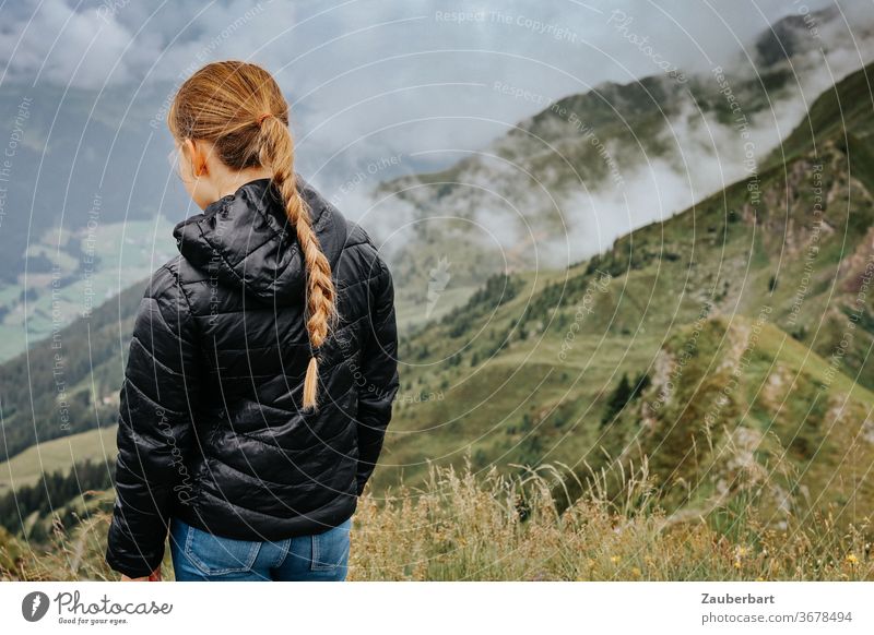 Mädchen mit Zopf schaut in ein Tal mit Wolken in den Alpen in Südtirol Kind blond beobachten Steppjacke klein schwarz Berge grün schauen Wandern Hand Profil