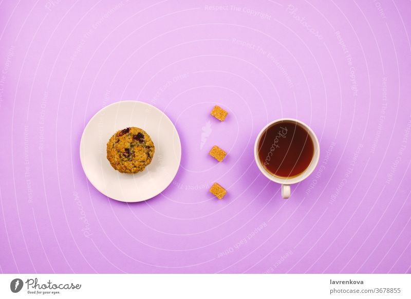 Flatlay mit einem Blaubeer-Muffin, einer Tasse Tee und Rohrzuckerwürfeln. Frühstückskonzept. Violetter Hintergrund. frisch Koffein Bäckerei violett trinken
