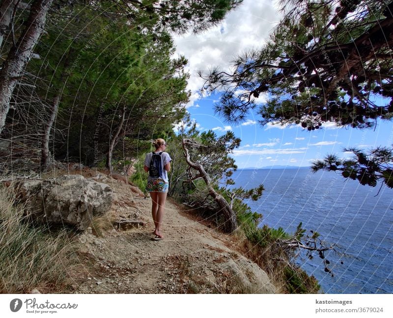 Junger aktiver Feamle-Tourist mit kleinem Rucksack, der auf einem Küstenweg zwischen Pinienbäumen wandert und nach einer abgelegenen Bucht sucht, um allein in Ruhe am Meer in Kroatien zu schwimmen. Reise- und Abenteuerkonzept.