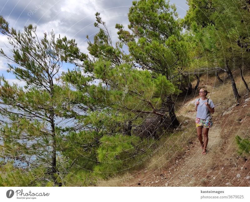 Junger aktiver Feamle-Tourist mit kleinem Rucksack, der auf einem Küstenweg zwischen Pinienbäumen wandert und nach einer abgelegenen Bucht sucht, um allein in Ruhe am Meer in Kroatien zu schwimmen. Reise- und Abenteuerkonzept.