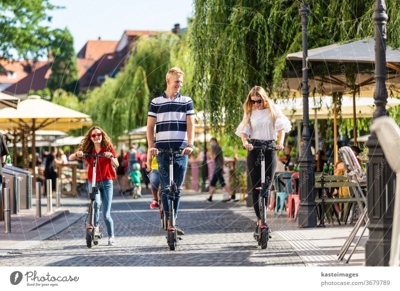 Trendige, modische Gruppe von Freunden, die auf öffentlichen Miet-Elektrorollern in der städtischen Umgebung fahren. Neuer umweltfreundlicher, moderner öffentlicher Stadtverkehr in Ljubljana, Slowenien