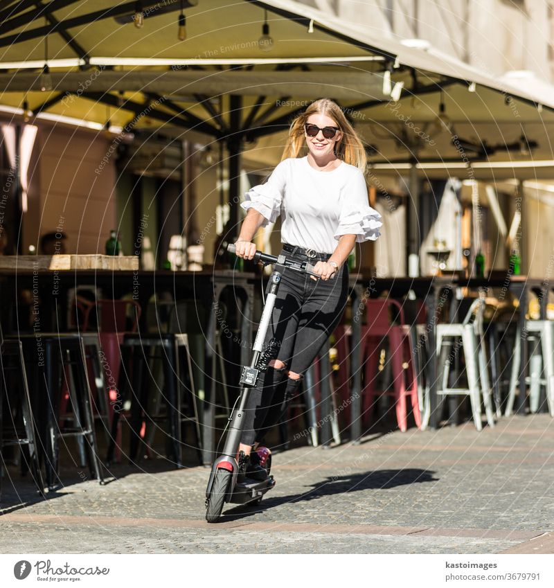 Trendige, modische Teenager-Mädchen fahren auf öffentlichen Leih-Elektrorollern im städtischen Umfeld. Neuer umweltfreundlicher, moderner öffentlicher Stadtverkehr in Ljubljana, Slowenien