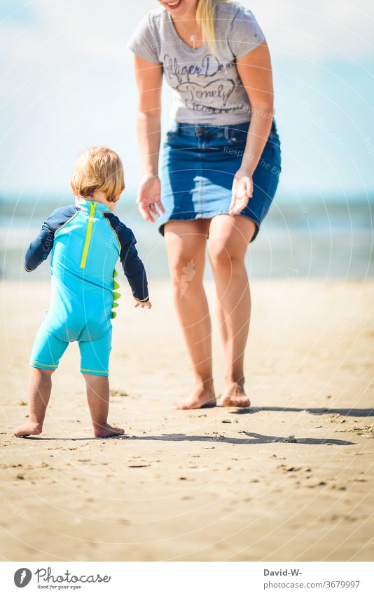 kleiner Junger läuft unsicher die ersten Schritte am Strand in die Arme der Mutter laufen gehen Gehversuche die ersten schritte Kind Kleinkind süß niedlich
