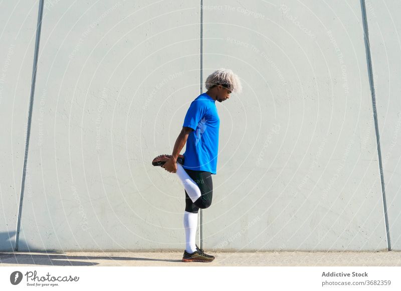 Afroamerikanischer Sportler beim Aufwärmen auf der Straße Übung Fitness Dehnung Training Gebäude Großstadt Wand männlich Gesundheit modern Athlet Beine