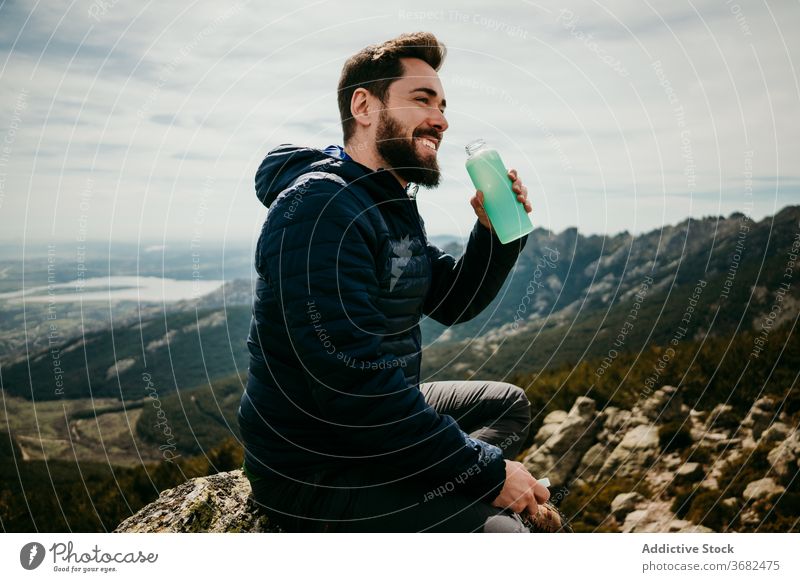 Glücklicher männlicher Reisender, der in den Bergen Wasser trinkt Mann Lächeln trinken Berge u. Gebirge ruhen Felsbrocken puerto de la morcuera Spanien heiter