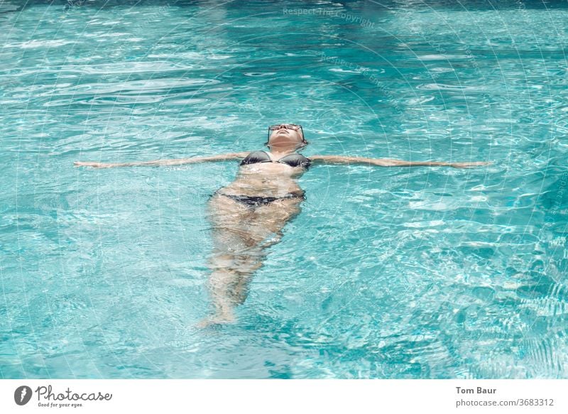 Einfach treiben lassen! Frau in schwarzen Bikini lässt sich auf dem Rücken im Pool treiben wasser frau bikini sonnenbrille Sommer schön sich[Akk] entspannen
