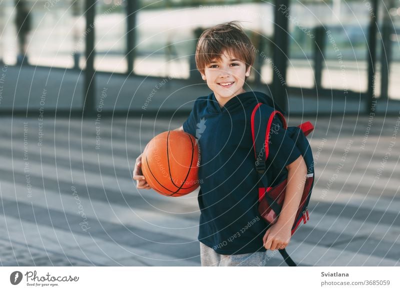 Porträt eines schönen Jungen in Sportuniform mit Rucksack und Basketball. Der Junge lächelt und hält den Ball in seinen Händen. Training, Erziehung, Sportunterricht