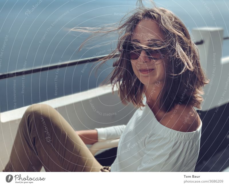 Porträt einer brünetten Frau mit wehenden Haaren und Sonnenbrille portät wehendes haar sonnenbrille Blick in die Kamera wehendes Haar lässig Außenaufnahme schön