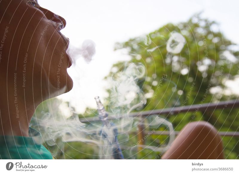 Jugendlicher raucht Shisha im Freien und bläst Rauchringe in die Luft Rauchen jugendlicher Wasserpfeifenrauch Freizeit Gesundheitsrisiko gesundheitsschädlich