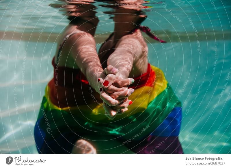 zwei Frauen am Pool zusammen mit einer regenbogenfarbigen Schwulenfahne umwickelt. LGBT-Konzept Liebe lesbisch Schwulenflagge unter Wasser Schwimmbad