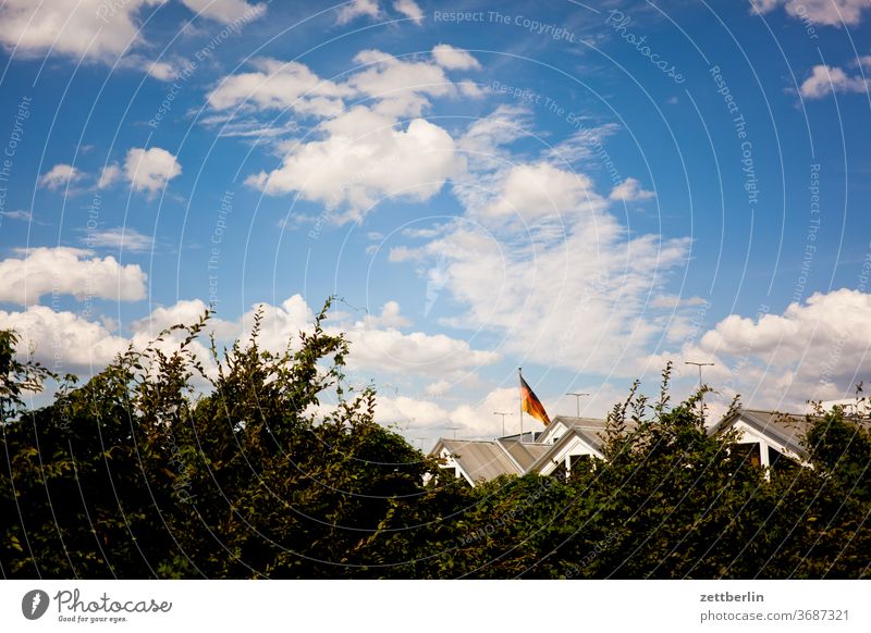 Dächer unter deutscher Fahne haus wohnhaus dorf stadt siedlung dach first wohngebiet hecke himmel wolken sommer fahne deutschland deutschlandfahne nation