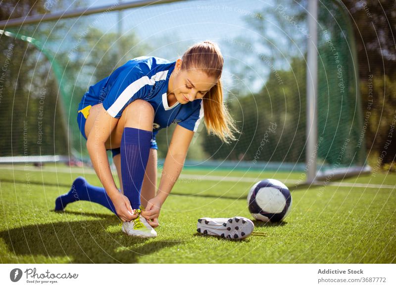 Positive Sportlerin beim Binden der Fußballschuhe Krawatte Stiefel Training vorbereiten positiv angezogen Feld Frau Athlet Ball Tor Sportbekleidung Gesundheit
