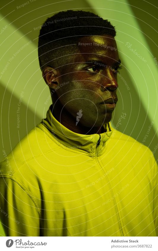 Ernster ethnischer Sportler im Studio mit Neonlicht Athlet selbstbewusst ernst Mann neonfarbig grün Schatten Bestimmen Sie Streifen brutal aktiv physisch jung