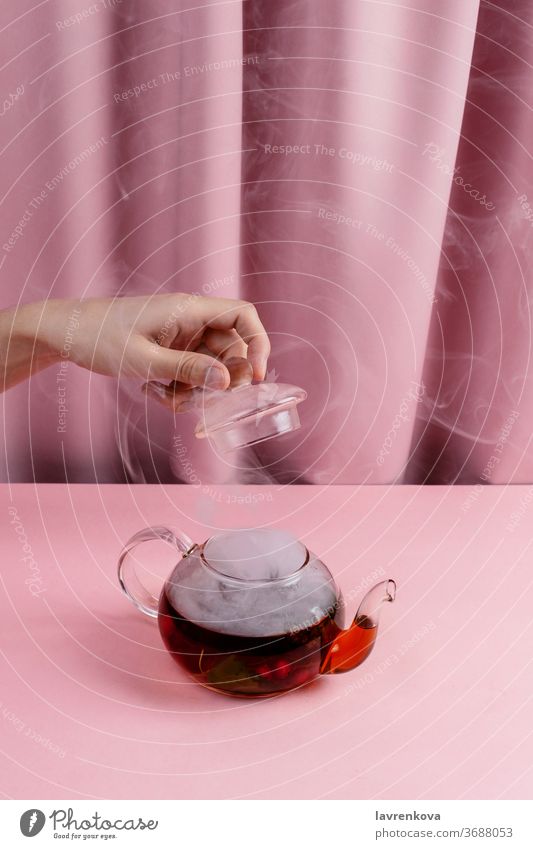 Frau hält den Teekannendeckel über dem Kessel mit dem dampfenden Früchte- und Beerentee in der Hand Getränk Wasserkessel Topf heiß Verdunstung Tisch Hygge
