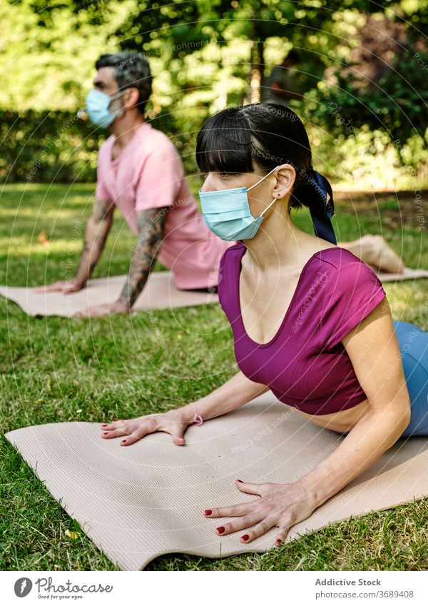 Paar macht Yoga in Cobra-Pose im Park Kobra-Pose Mundschutz Coronavirus Zusammensein ruhig beweglich sich[Akk] entspannen Partnerschaft grün Harmonie Ausbruch