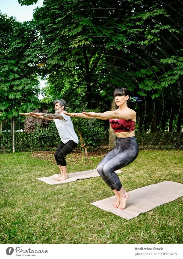 Fokussierte Paar tun Yoga in Awkward Pose im Park ungünstige Haltung Gleichgewicht Asana Körperhaltung utkatasana Zusammensein Unterlage grün Garten Gesundheit