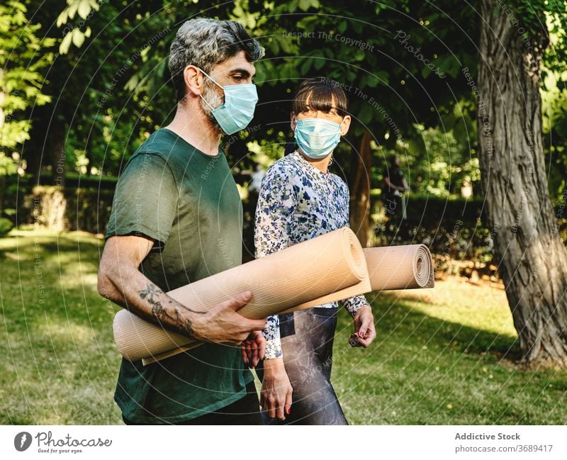 Fröhliches Paar mit medizinischen Masken und Yoga-Matten zu Fuß im Park Unterlage Mundschutz Spaziergang heiter Zusammensein Coronavirus COVID Pandemie COVID19