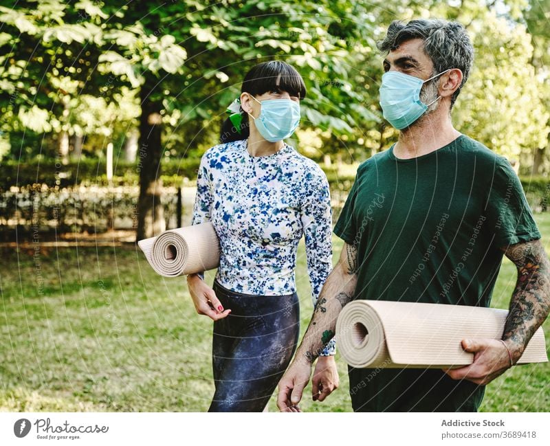Fröhliches Paar mit medizinischen Masken und Yoga-Matten zu Fuß im Park Unterlage Mundschutz Spaziergang heiter Zusammensein Coronavirus COVID Pandemie COVID19