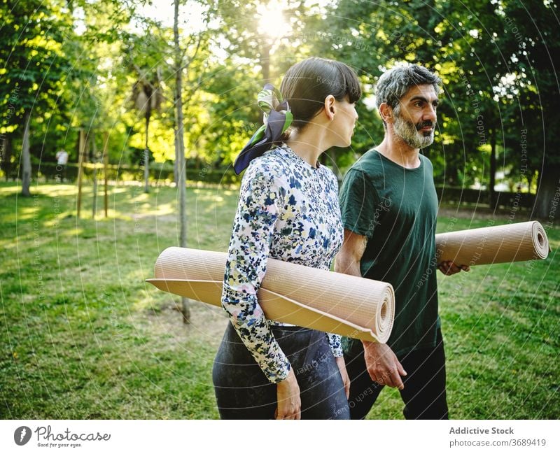 Fröhliches Paar mit Yoga-Matten zu Fuß im Park Unterlage Spaziergang heiter Zusammensein positiv reden Glück Kommunizieren Gespräch üben Wellness Aktivität