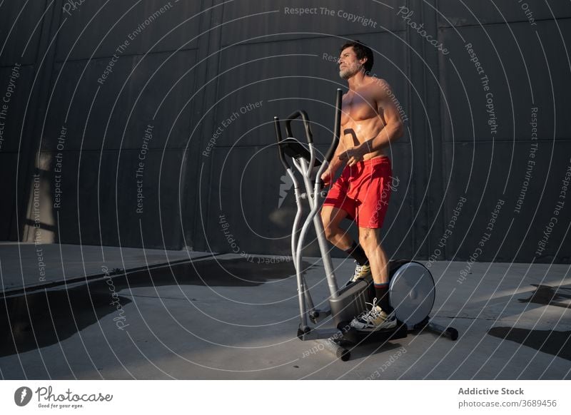 Sportler trainiert auf Stepper auf der Straße Maschine Übung Herz Training Großstadt elliptisch Athlet männlich muskulös stark nackter Torso ohne Hemd passen