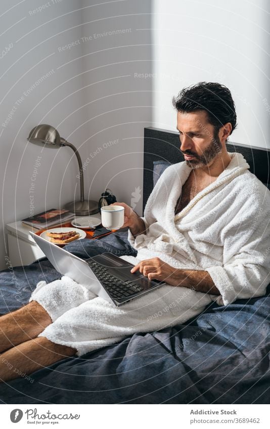 Ruhiger Mann beim Frühstück im Bett freiberuflich Kaffee Laptop Arbeit abgelegen Bademantel benutzend männlich Geschäftsmann Tasse frisch Morgen trinken Gerät