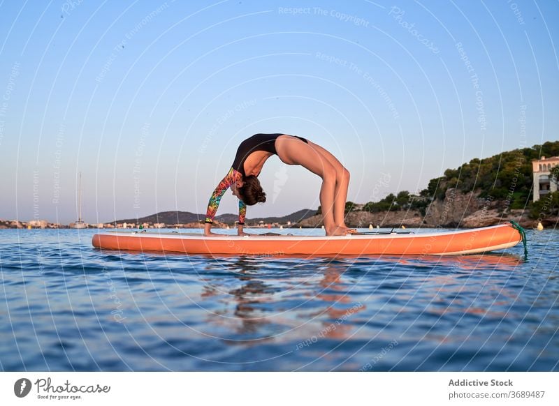 Flexible weibliche Surfer tun Yoga in Rad-Pose Radstellung üben Frau Asana beweglich Paddelbrett MEER Harmonie Badeanzug Abend Dämmerung Sonnenuntergang