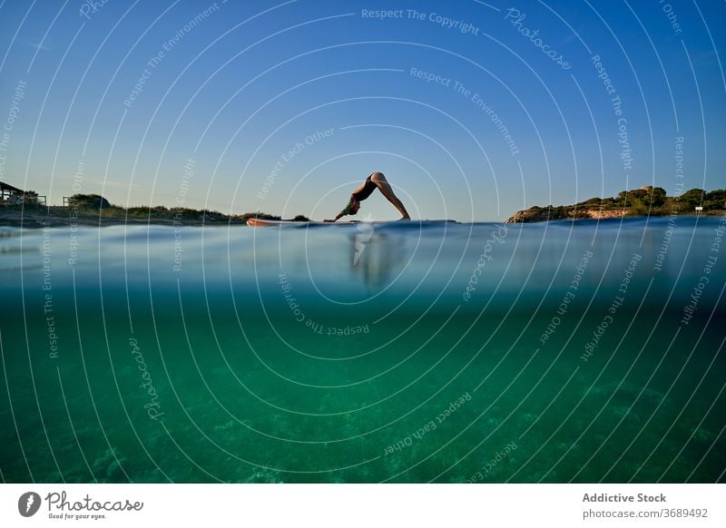 Flexible Frau macht Yoga auf Paddleboard Sonnenuntergang Pose Surfer Paddelbrett adho mukha svanasana Gleichgewicht MEER Wasser Gesundheit Natur Harmonie