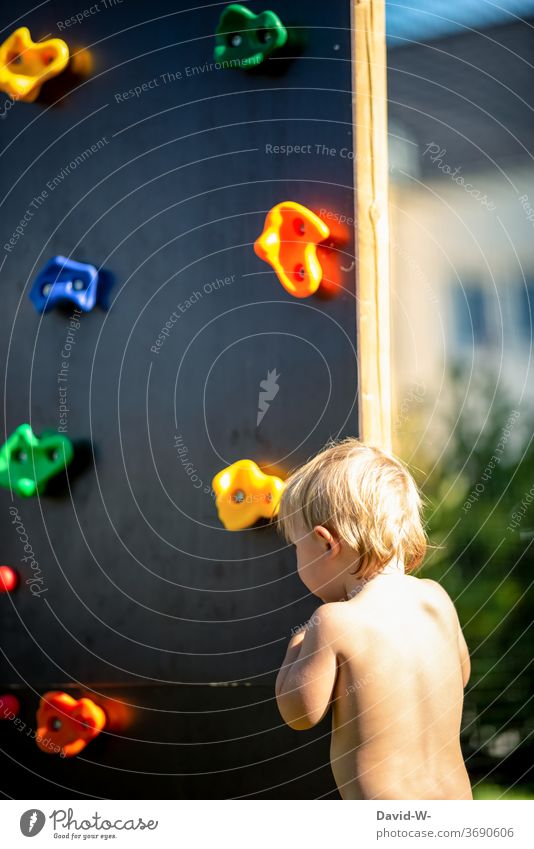 Kind steht vor einer Kletterwand spielen klettern Kindheit Spielplatz Sommerlich sommer hitze Junge ängstlich schüchtern vorsichtig