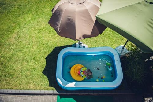 Kind badet im Garten in einem Planschbecken umringt von Sonnenschirmen die Schatten spenden schattenspender Sonnig Quarantäne Eigenheim Kindheit Mädchen baden