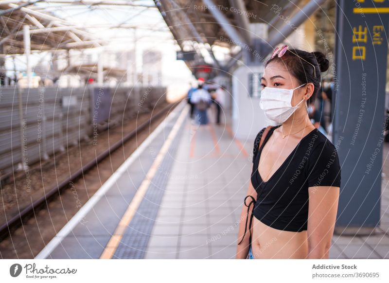 Ethnische Frau auf Bahnsteig Podest Eisenbahn Station warten Mundschutz Coronavirus COVID medizinisch neue Normale ethnisch asiatisch Passagier Ausbruch Seuche