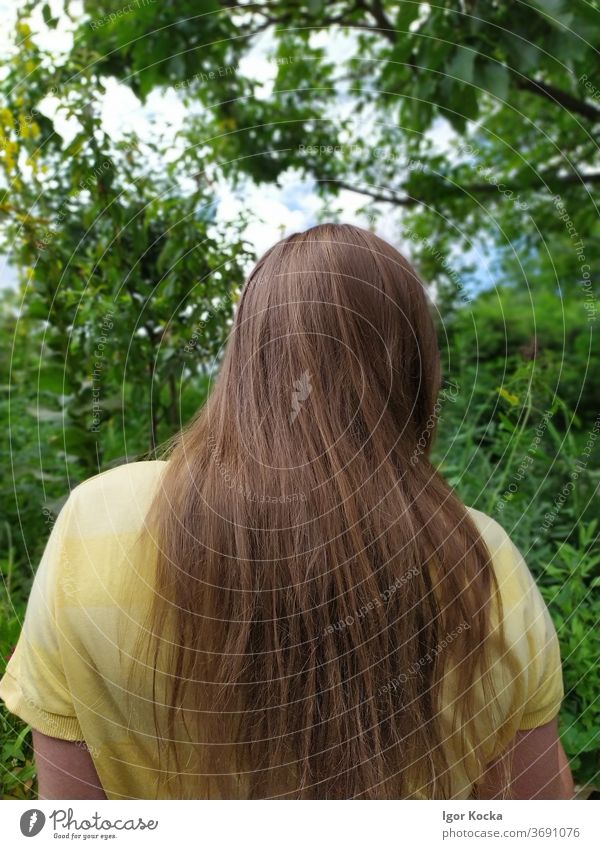 Rückansicht einer im Garten stehenden Frau Bäume grün gelb langhaarig Kopf Oberkörper brünett Schwache Tiefenschärfe Zentralperspektive Erholung