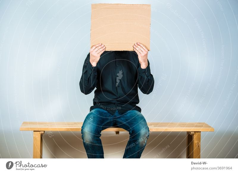 Mann hält ein Schild vor sein Gesicht sitzend wartenWartezimmer pappkarton Platzhalter Textfreiraum neutral anonym männlich Mensch Leben Farbfoto