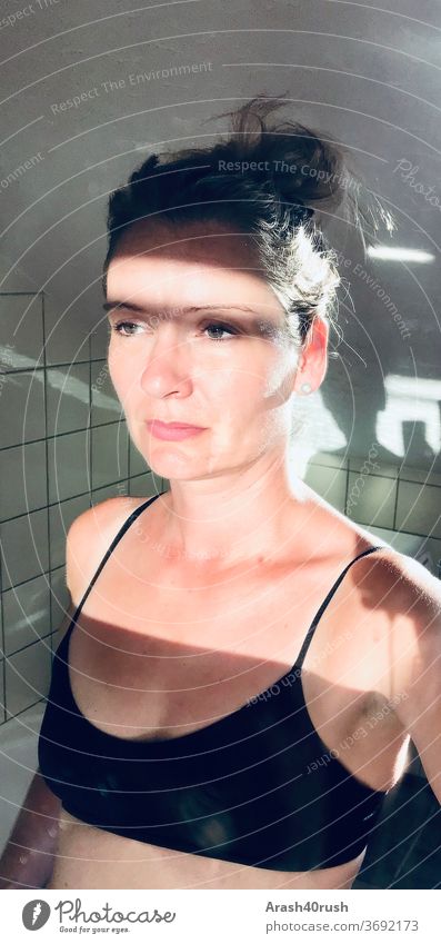 Junge Frau im Badezimmer geblendet von der Sonne im Spiegel Farbfoto Düster Blick nachdenklich Licht/Schattenspiel feminin Erwachsene Innenaufnahme ohne Blitz