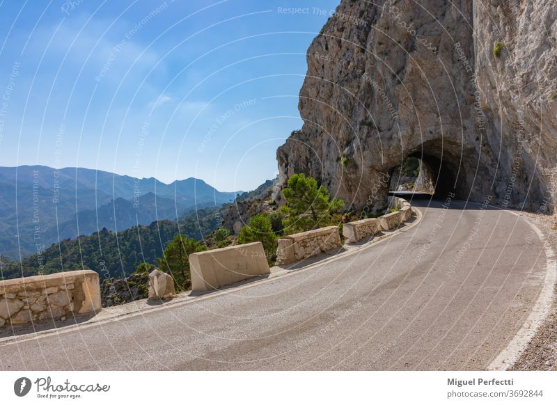 Schmale Hochgebirgsstraße mit einem Tunnel aus Stein und Blick auf andere Gipfel, ist bekannt als Carretera de la Cabra, Granada, Spanien. Straße Landschaft