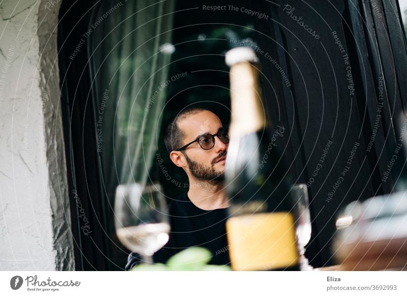 Ein Mann beim Day Drinking mit einer Flasche Prosecco und Gläsern an einen Tisch. Alkohol Sekt Garten Sektglas Tag Glas Getränk alkoholkonsum Brille braunhaarig