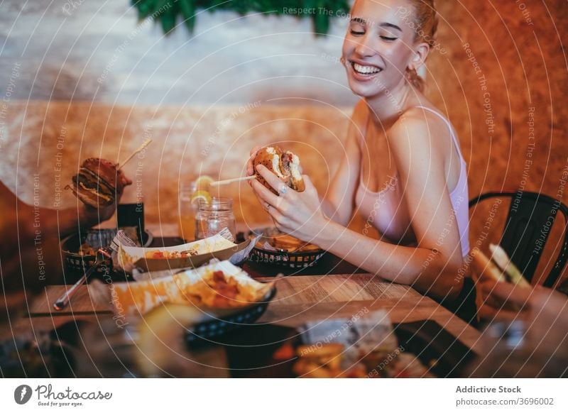 Glückliche junge Frau isst Burger im Café essen Spaß haben Fastfood heiter Freund Zusammensein Hamburger Lachen Lifestyle Freundschaft Sitzung Kommunizieren