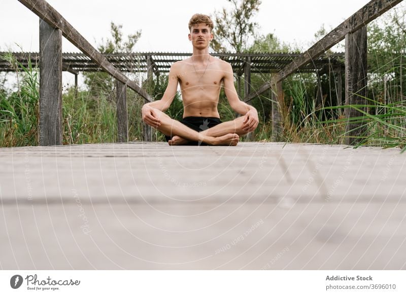 Mann meditiert in Lotus-Pose meditieren Yoga Achtsamkeit Stressabbau Natur ruhig Harmonie Windstille männlich hölzern Spazierweg Gesundheit üben sitzen