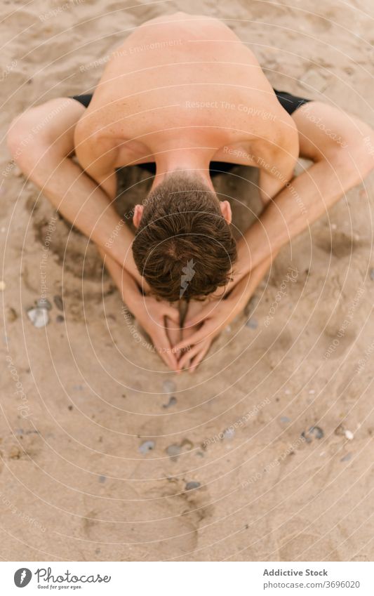 Fokussierter Mann macht Yoga am Strand üben Sand Asana sitzen gebundener Winkel baddha konasana Wegbiegung weitergeben männlich Yogi schlank ohne Hemd