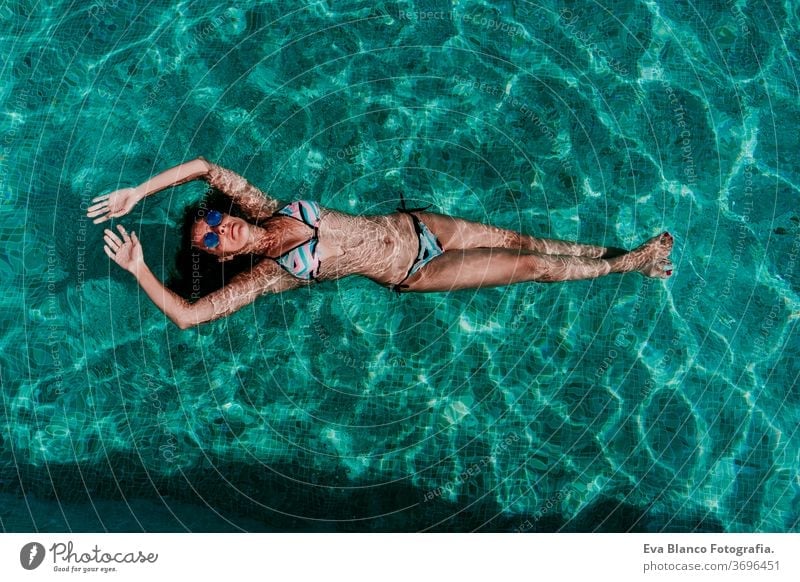 Draufsicht auf eine glückliche junge Frau, die in einem Pool schwebt. Sommer und lustiger Lebensstil unter Wasser Schwimmsport Blasen Spaß Kaukasier Sinkflug